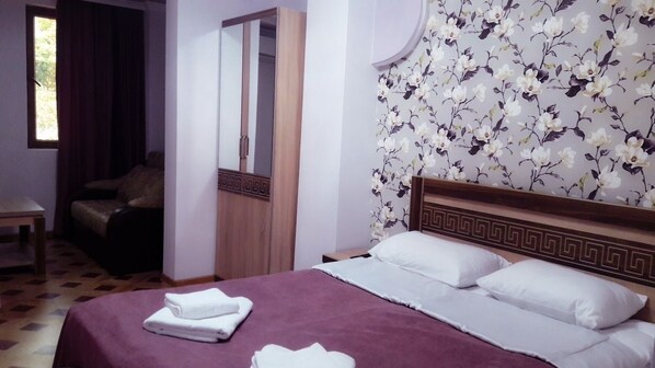 A hotel room with a bed, a mirror, a wardrobe, and a floral wallpaper.