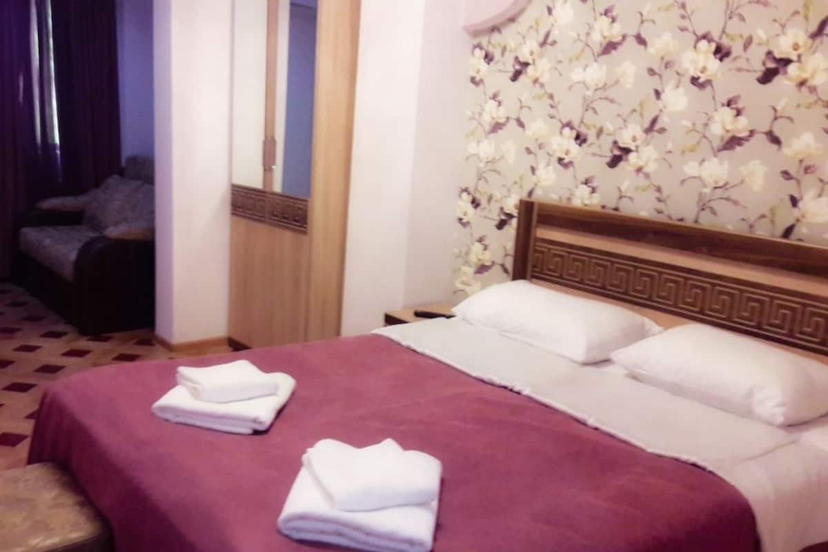 A hotel room with a bed, a wooden headboard, a mirror, and a floral wallpaper.