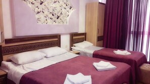 A hotel room with two beds, each with a purple bedspread and white pillows. There is a wooden headboard with a decorative pattern, a wardrobe, and a large floral artwork on the wall. - Georgian Palace (Kutaisi)