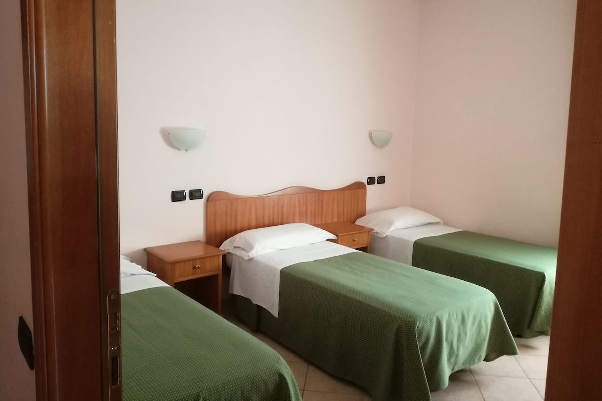 A hotel room with two single beds, a wooden headboard, bedside tables, and wall-mounted lamps.