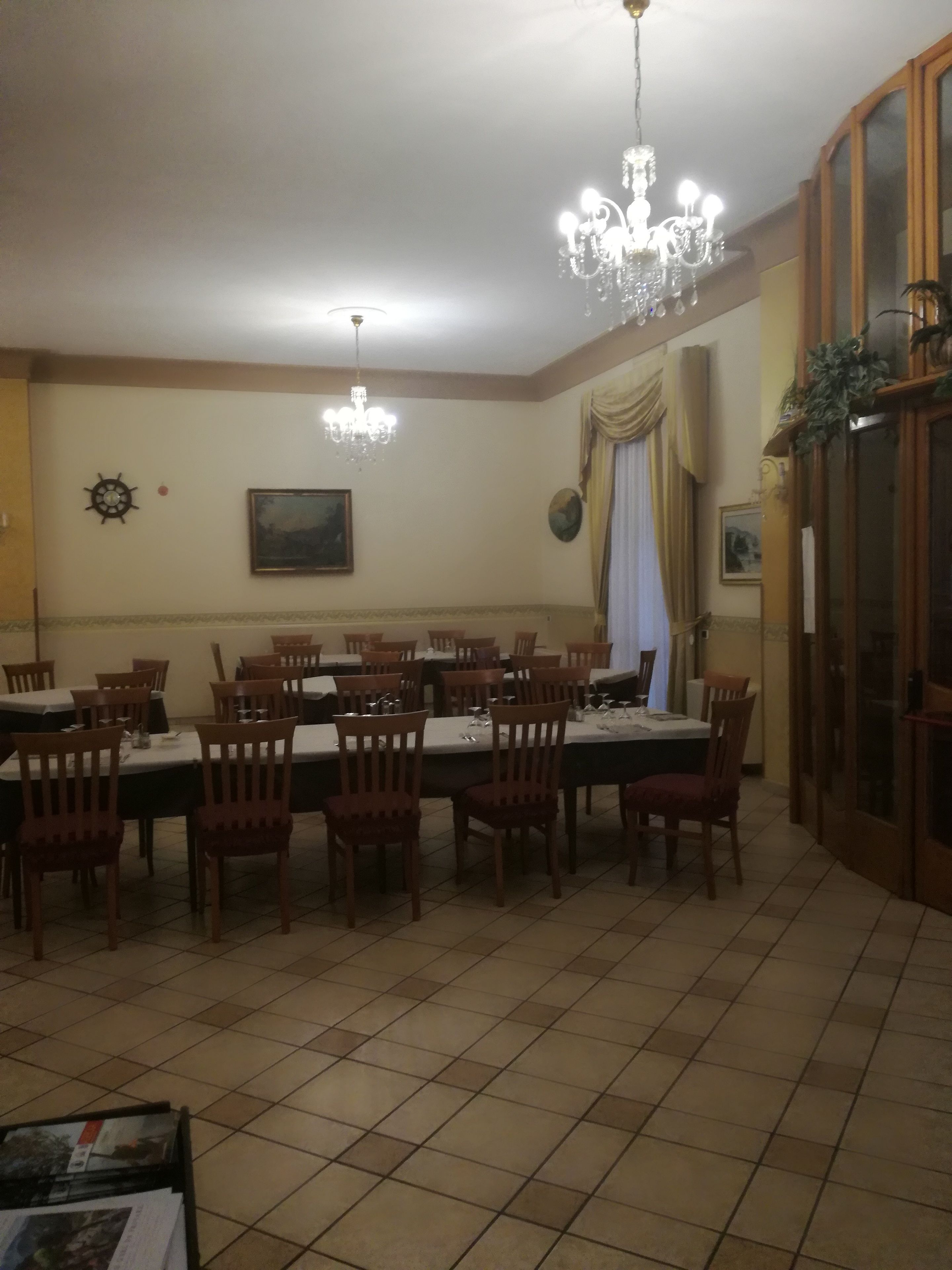 A dining area with multiple tables and chairs, a chandelier, and a clock on the wall.