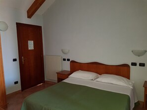 A bedroom with a wooden headboard, a green bedspread, a white pillow, a bedside table, a nightstand, a radiator, and a door with a sign. - Hotel Gentile (Agerola)