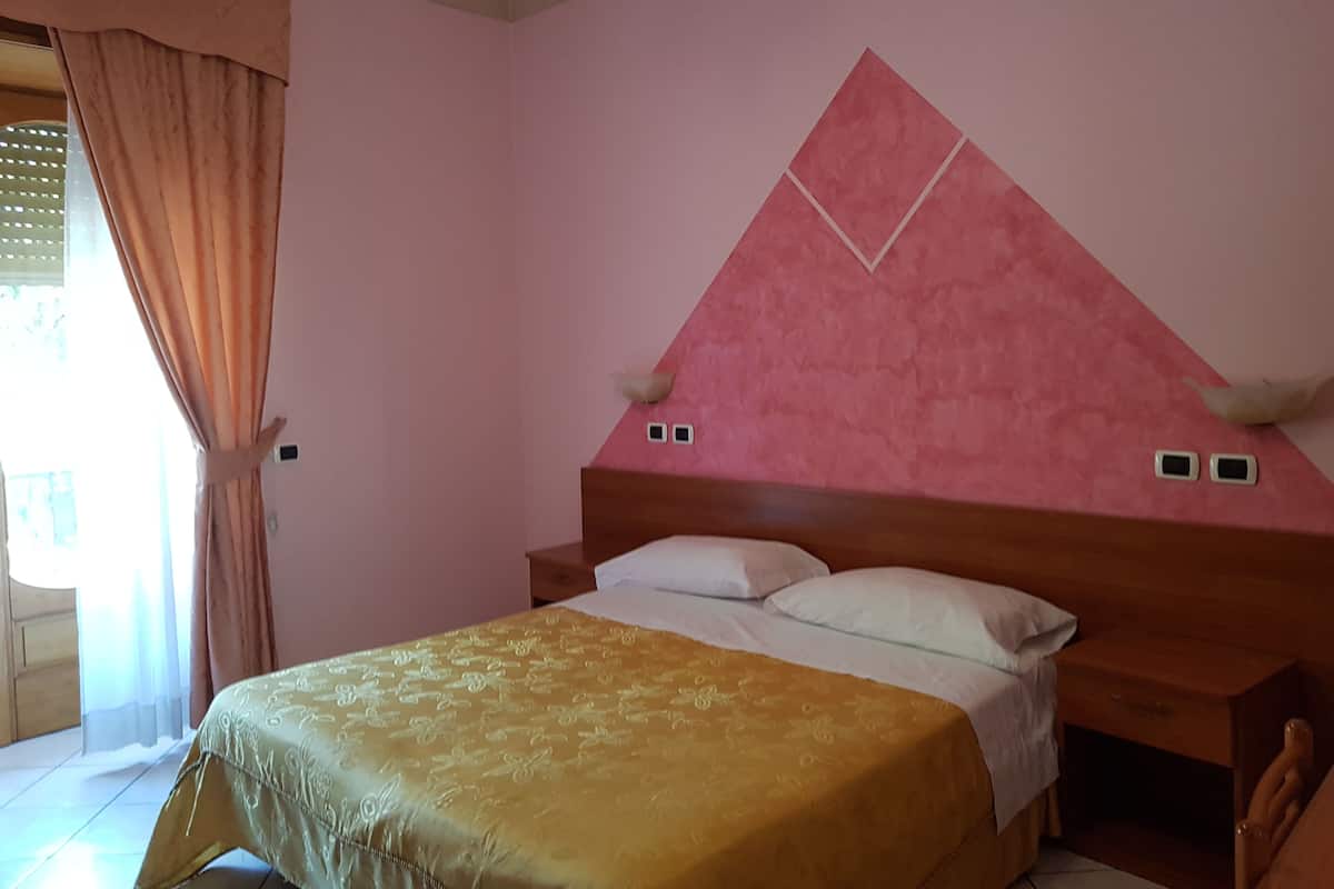 A bedroom with a bed, a wooden headboard, and a pink wall with a geometric design.