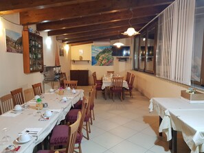 Un comedor con mesas y sillas de madera, un televisor montado en la pared y un cuadro en la pared.