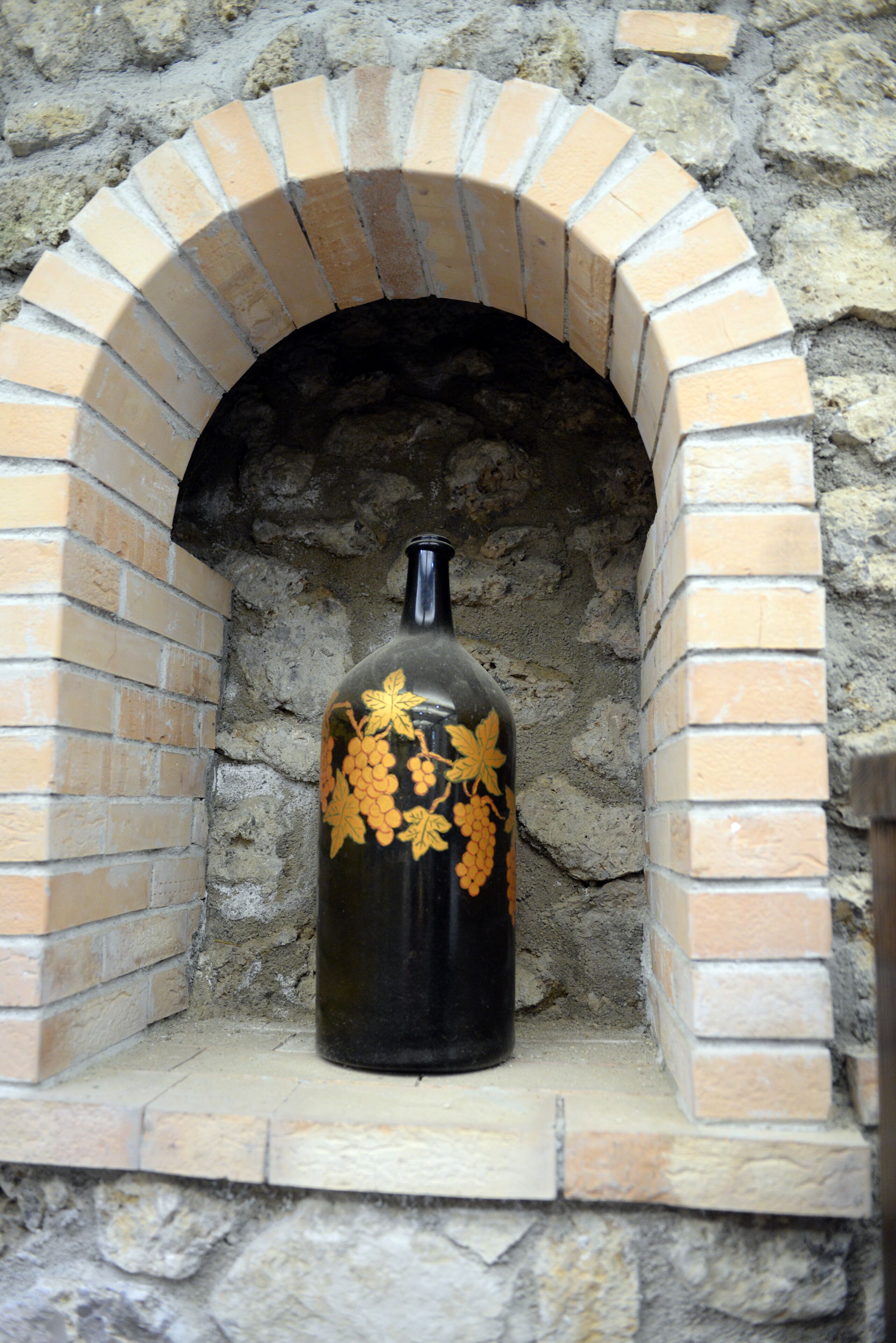 A bottle with a grapevine design in a brick oven alcove.