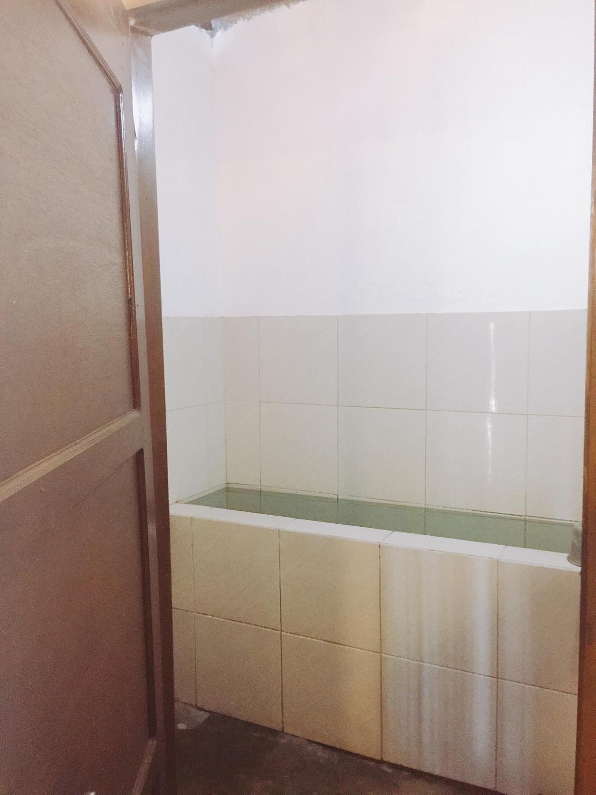 A bathroom with a tiled wall, a glass shower enclosure, and a wooden door.