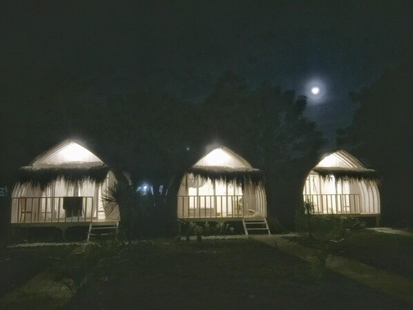 Trois huttes à toits de chaume, avec la lune en arrière-plan.