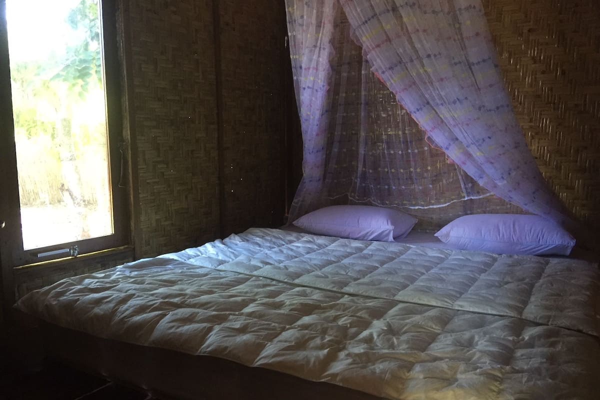 Una cama con dosel, una ventana con vistas a la vegetación y un muro de ladrillo.