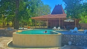 A swimming pool with a stone wall and a covered area with chairs. - Maleo Moyo Seaside Resort (Moyo)