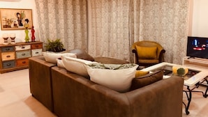 Un salon avec un canapé marron, un fauteuil jaune, un téléviseur et un rideau à motifs.