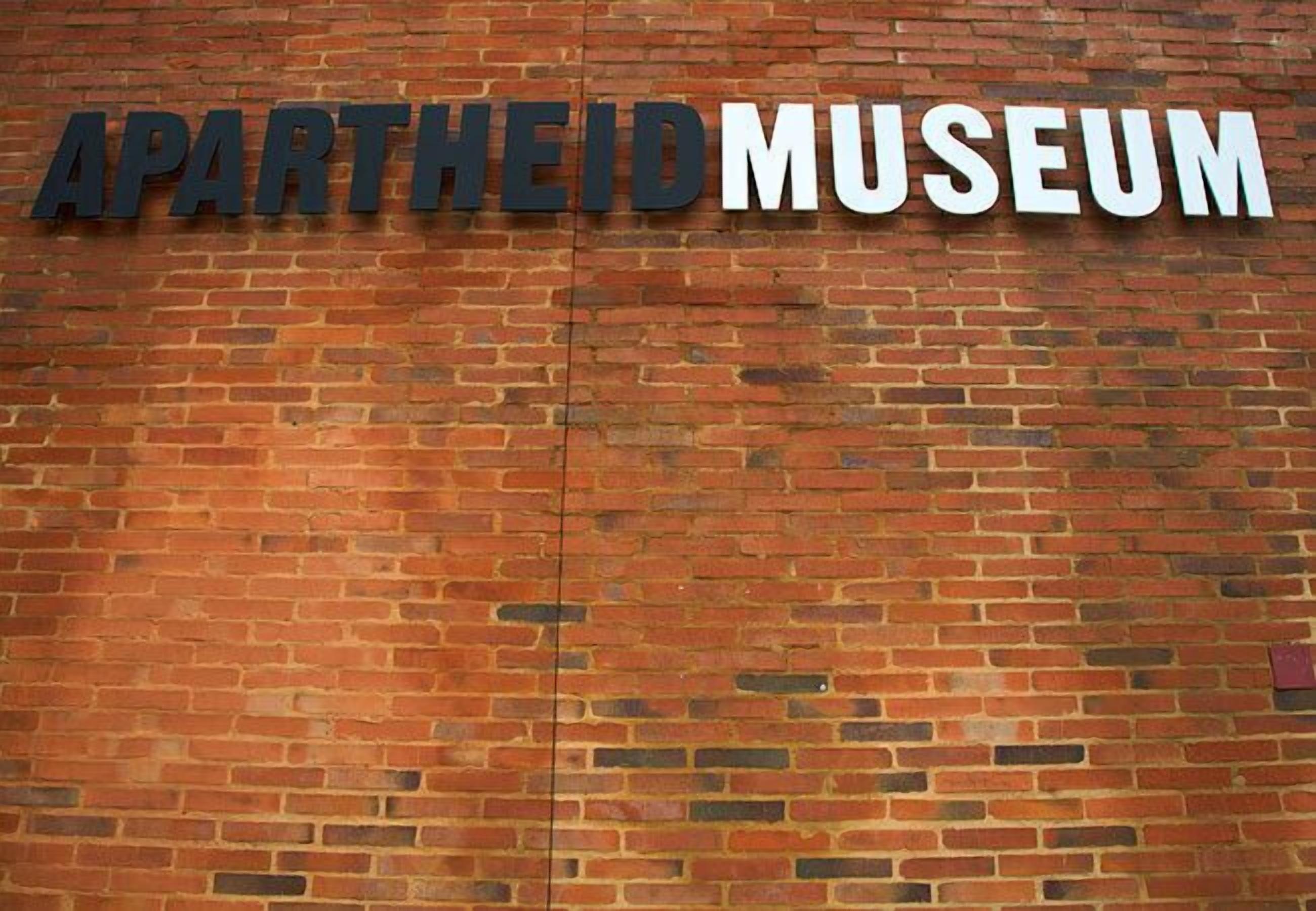 Eine Backsteinmauer mit den großformatigen, fetten Schriftzügen "APARTHEID MUSEUM".