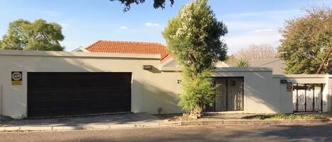 A residential building with a garage, a gated entrance, and a small tree in front.