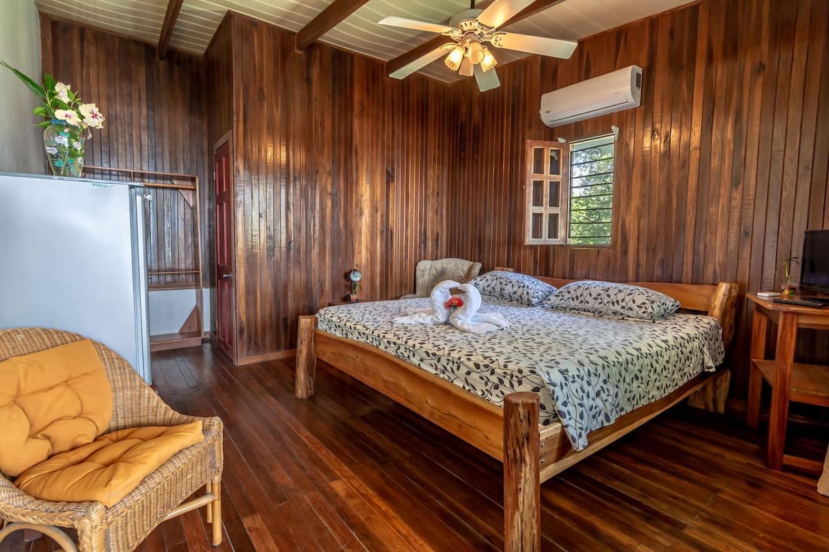 A wooden-paneled room with a bed, a chair, a desk, and a ceiling fan.