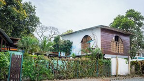 A two-story building with a white facade and brown roof, surrounded by greenery and a metal fence. - Cabinas Arrecife (Cahuita)