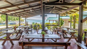 An outdoor seating area with wooden tables and benches, overlooking a body of water. - Cabinas Arrecife (Cahuita)