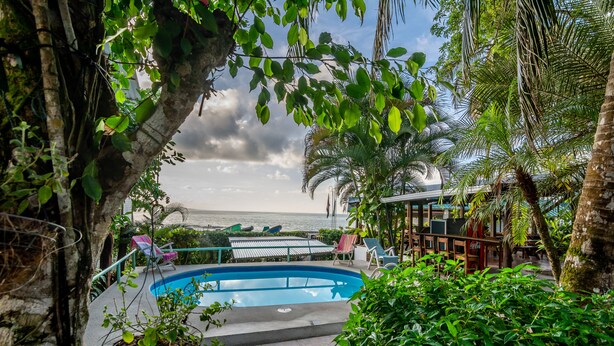 A pool area with lounge chairs and a view of the sea. - Cabinas Arrecife (Cahuita)