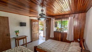 A bedroom with two wooden beds, a ceiling fan, a TV mounted on the wall, and a window with curtains. - Cabinas Arrecife (Cahuita)