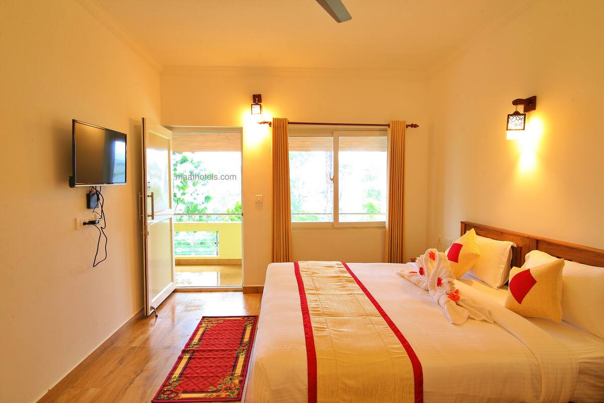 Una habitación de hotel con una cama, un televisor montado en la pared, una ventana con cortinas y una puerta que da a un espacio al aire libre.
