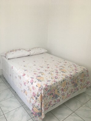 Una cama con una colcha estampada y dos almohadas en una habitación con suelo de baldosas.