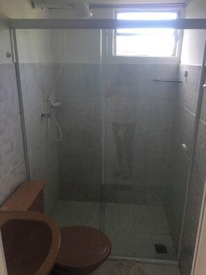 Un box de ducha pequeño y cerrado con puerta de vidrio, un inodoro y una ventana sobre la ducha.