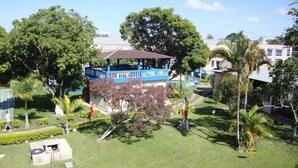 A building with a blue exterior and a covered area, surrounded by greenery and palm trees. - Pousada Clube Santa Cruz (Santa Cruz de Minas)