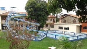 A swimming pool with a blue and white fence, a water slide, and a palm tree. - Pousada Clube Santa Cruz (Santa Cruz de Minas)