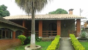 A house with a tiled roof, a porch, and a well-maintained garden with a pathway. - Pousada Clube Santa Cruz (Santa Cruz de Minas)