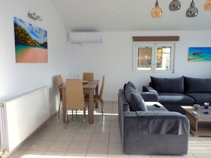 A modern living room with a dining area, grey sofa, and a painting of a beach.