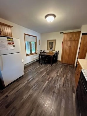 A kitchen with a refrigerator, wooden cabinets, a dining table with chairs, and a window.