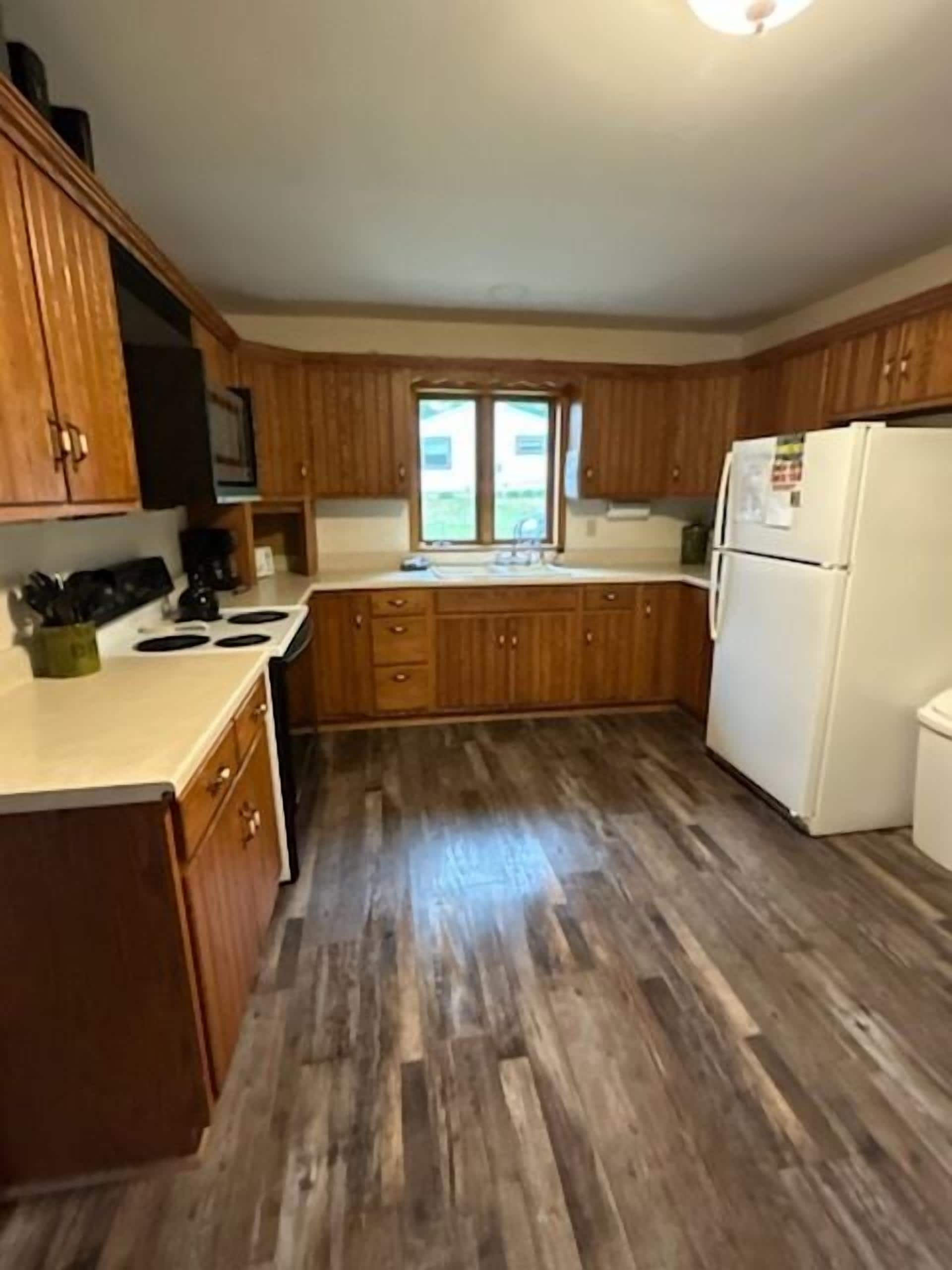 A kitchen with wooden cabinets, a white refrigerator, and a window.