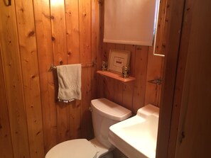 Un baño pequeño con paneles de madera, que incluye un inodoro, un lavamanos y una toalla colgada en un perchero.