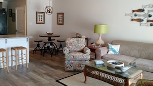 A living room with a floral armchair, a sofa, a coffee table, and a dining area with stools and a table. - Modern Beach Property recently updated (Surfside Beach)
