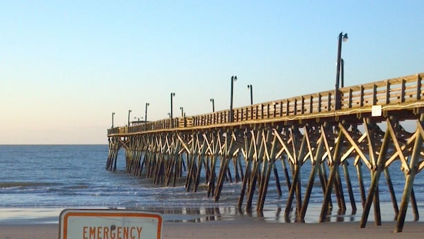 A beach with a pier in the background and a sign that reads "EMERGENCY ACCESS NO SUNBATHING BETWEEN SIGNS KEEP CLEAR". - Modern Beach Property recently updated (Surfside Beach)