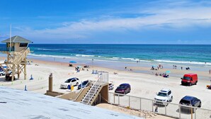 Ein Strand mit einem Rettungsturm, Strandliegen und Autos, die im Sand geparkt sind.