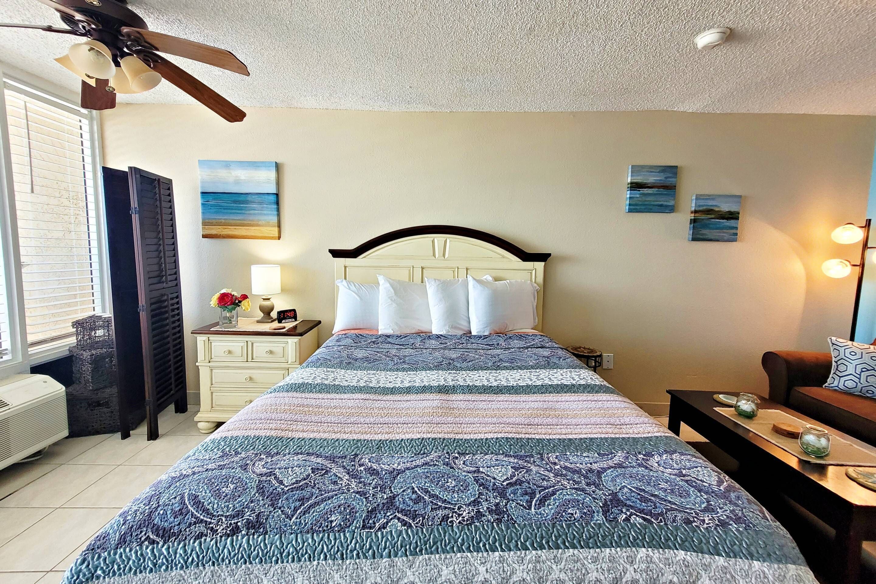 Une chambre à coucher comprenant un lit, une table de chevet, une commode et un ventilateur de plafond.