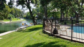 A park with a swimming pool, a river, and a fenced area with benches.