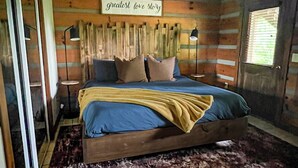 A bedroom with a bed, a ceiling fan, a wooden headboard, a window with blinds, and a sign on the wall.