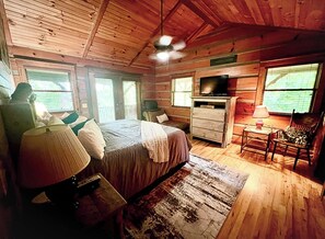 A wooden cabin bedroom with a bed, dresser, television, and a chair.