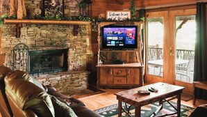 A cozy cabin interior with a stone fireplace, leather sofa, wooden coffee table, and a television.