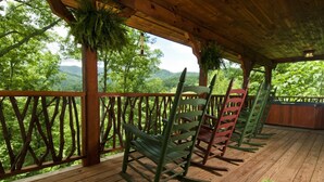 A wooden deck with rocking chairs and a wooden railing overlooking a forested landscape.
