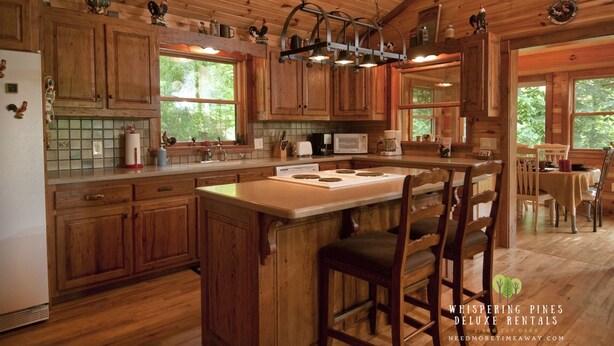 A rustic kitchen with wooden cabinets, a central island with bar stools, a microwave, and a coffee maker.