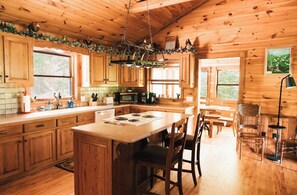 A wooden cabin kitchen with a central island, wooden cabinets, and a hanging light fixture.