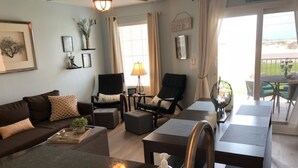 A modern living room with a sofa, armchairs, a coffee table, and a kitchen area with a sink and countertop. - 🔥 Beautifully Remodeled Grand Beach LOWEST Rates 🦀 Pool & Heated HotTub👙 (Gulf Shores)