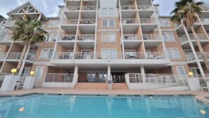 A multi-story hotel with balconies, a swimming pool, and palm trees. - 🔥 Beautifully Remodeled Grand Beach LOWEST Rates 🦀 Pool & Heated HotTub👙 (Gulf Shores)