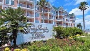 A multi-story hotel with balconies, a sign reading "The Grand Beach Resort," and landscaped gardens with various plants. - 🔥 Beautifully Remodeled Grand Beach LOWEST Rates 🦀 Pool & Heated HotTub👙 (Gulf Shores)