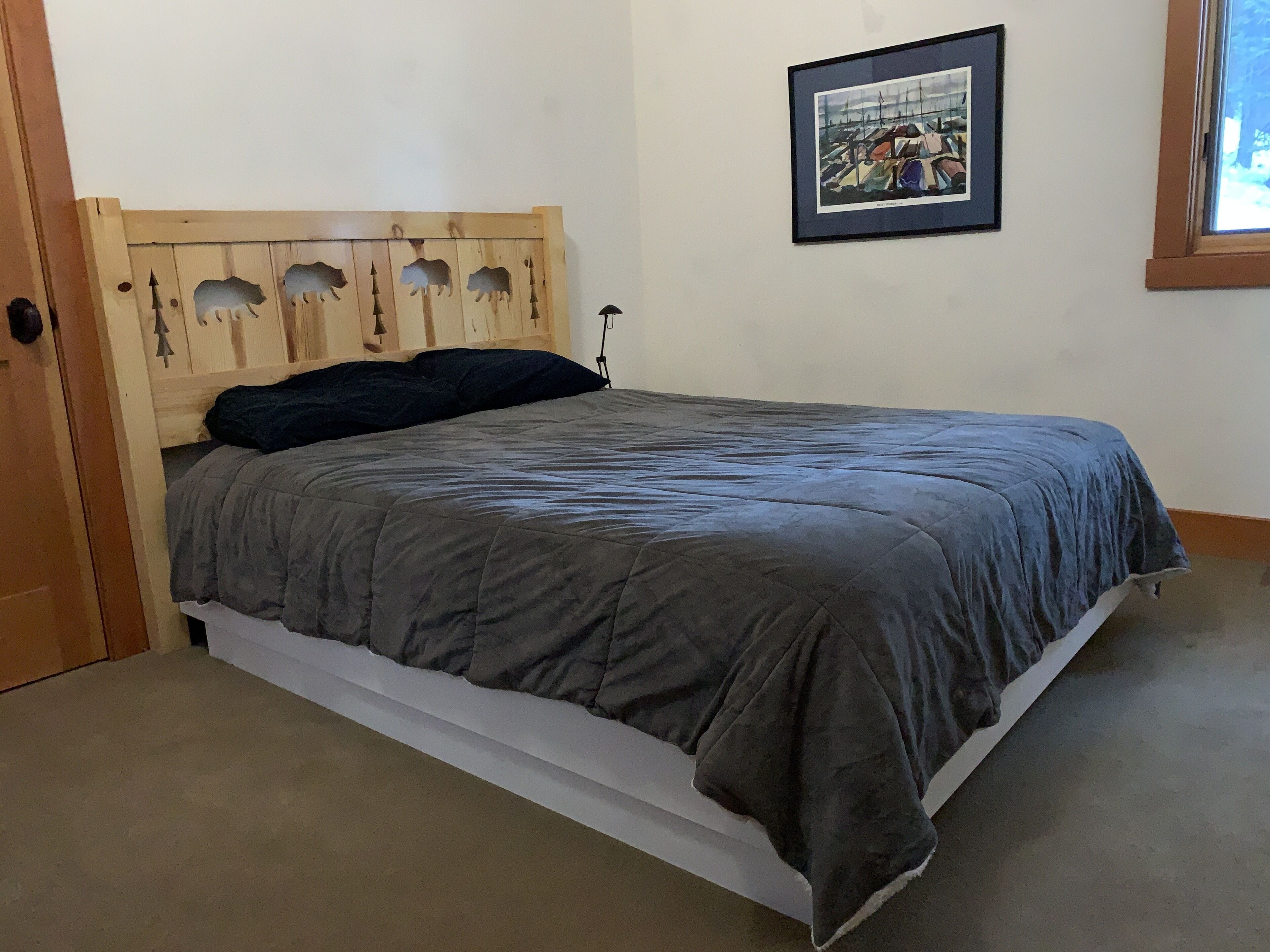 Uma cama com cabeceira de madeira, um quadro na parede e uma janela com vista para barcos.