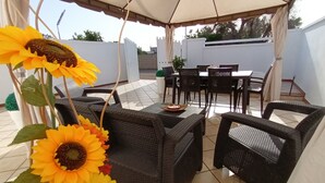 An outdoor patio with wicker furniture, a dining table, and chairs. Sunflowers are in a vase. -  Full comfort cottage a few steps from the sea and from the center (porto cesareo)