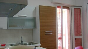 A kitchen with a sink, a wooden cabinet, and a window with a red curtain. -  Full comfort cottage a few steps from the sea and from the center (porto cesareo)