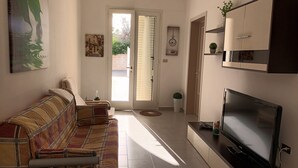 A living room with a sofa, a flat-screen TV, and a door leading outside. -  Full comfort cottage a few steps from the sea and from the center (porto cesareo)