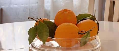 A clear glass bowl with oranges and leaves on a white table.